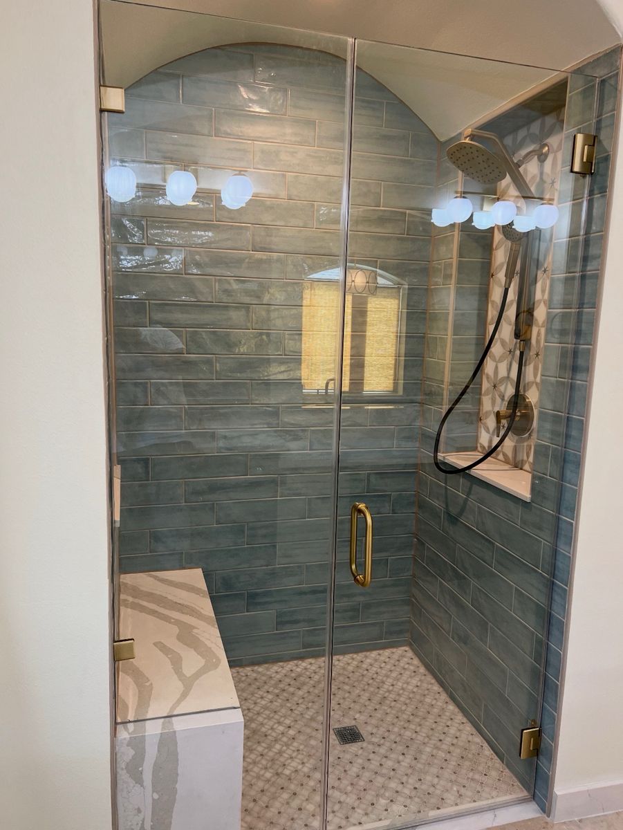 Finished arched walk-in shower with blue-green tile, glass door, and marble bench