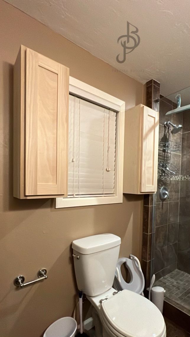Built-in wall cabinets flanking a window, with a dark-tile walk-in shower