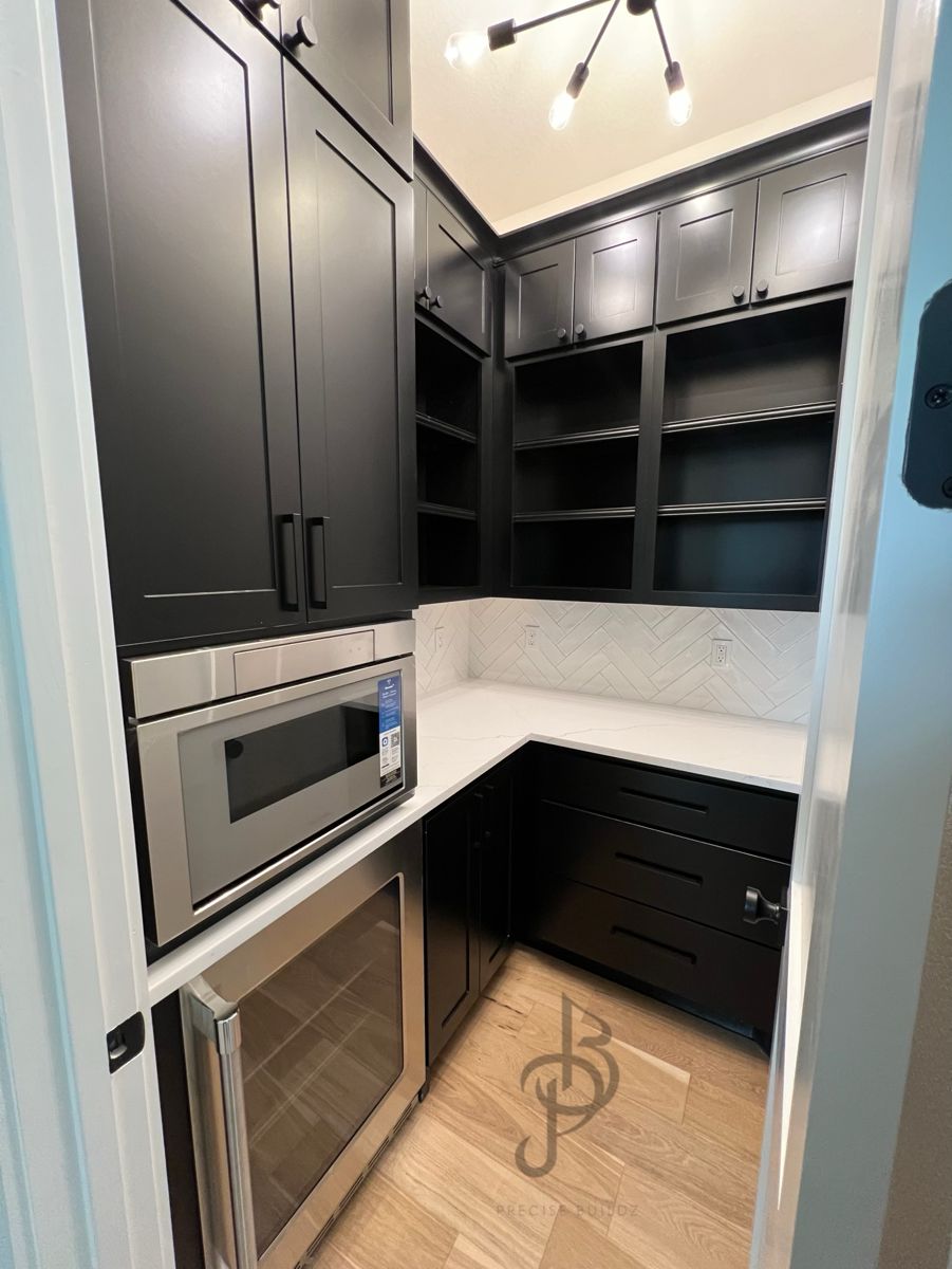 Corner view of a black shaker butler's pantry with quartz counters, herringbone backsplash, and luxury vinyl plank floors