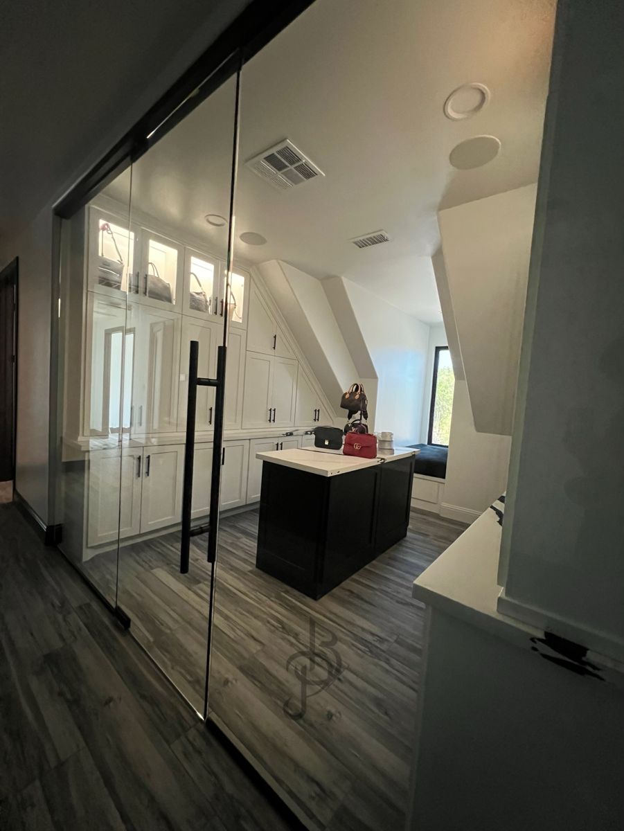Boutique walk-in closet seen through frameless glass doors, with a center island and window seat