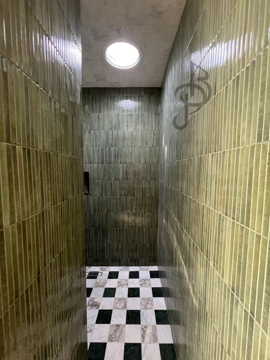 Walk-in shower with green vertical stacked tile, marble ceiling, skylight, and checkerboard marble floor