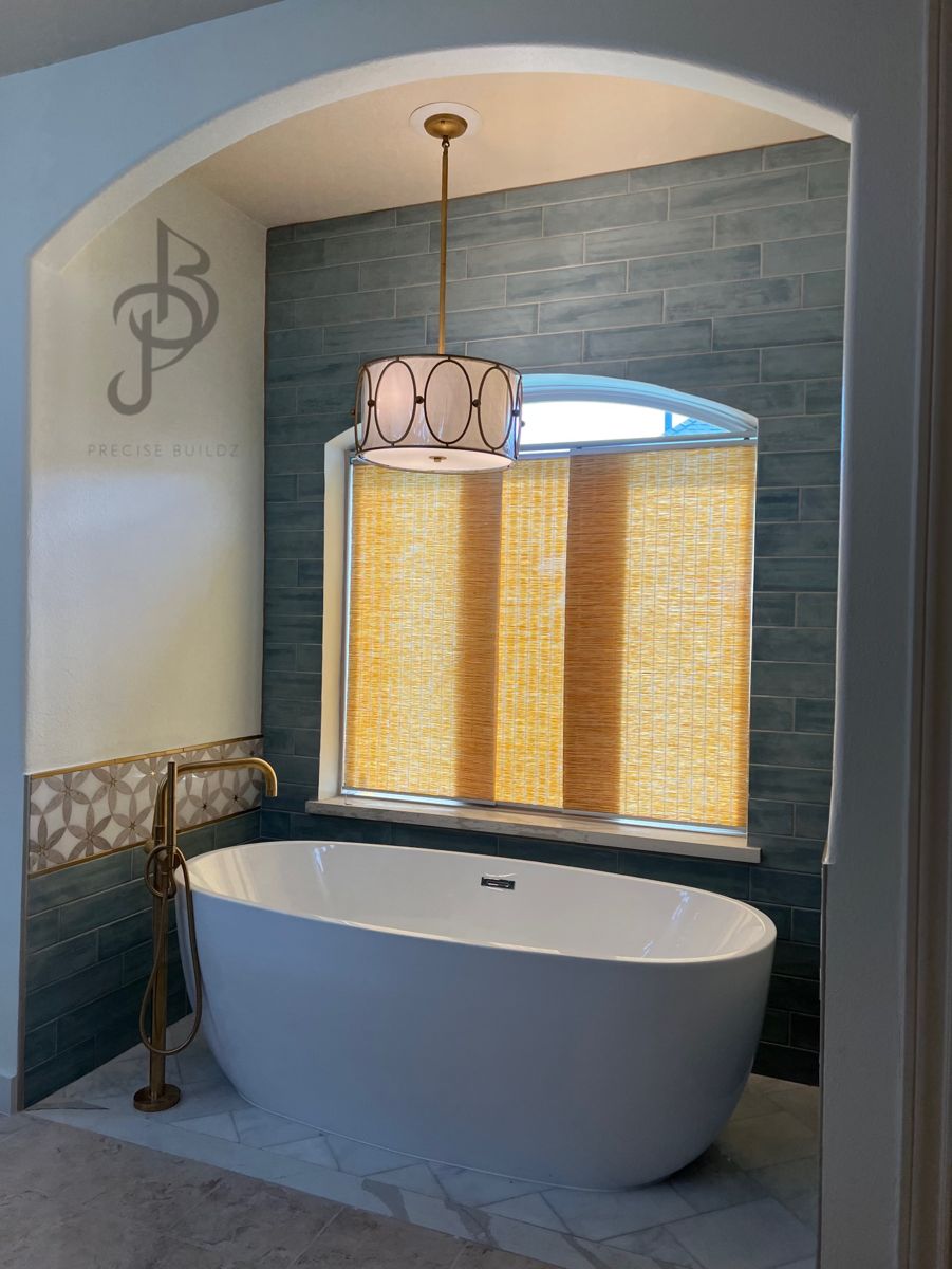 Renovated master bathroom with a freestanding soaking tub, teal tile, and brass fixtures