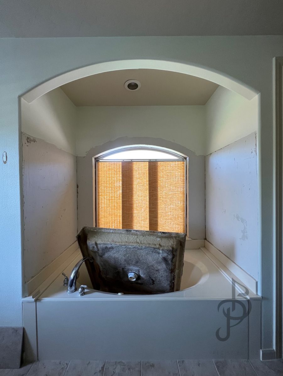 The same master bath tub alcove before renovation, with a dated drop-in tub and bare walls