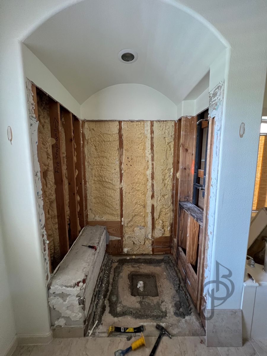 Structural stage showing a gutted room with exposed wall studs and spray-foam insulation
