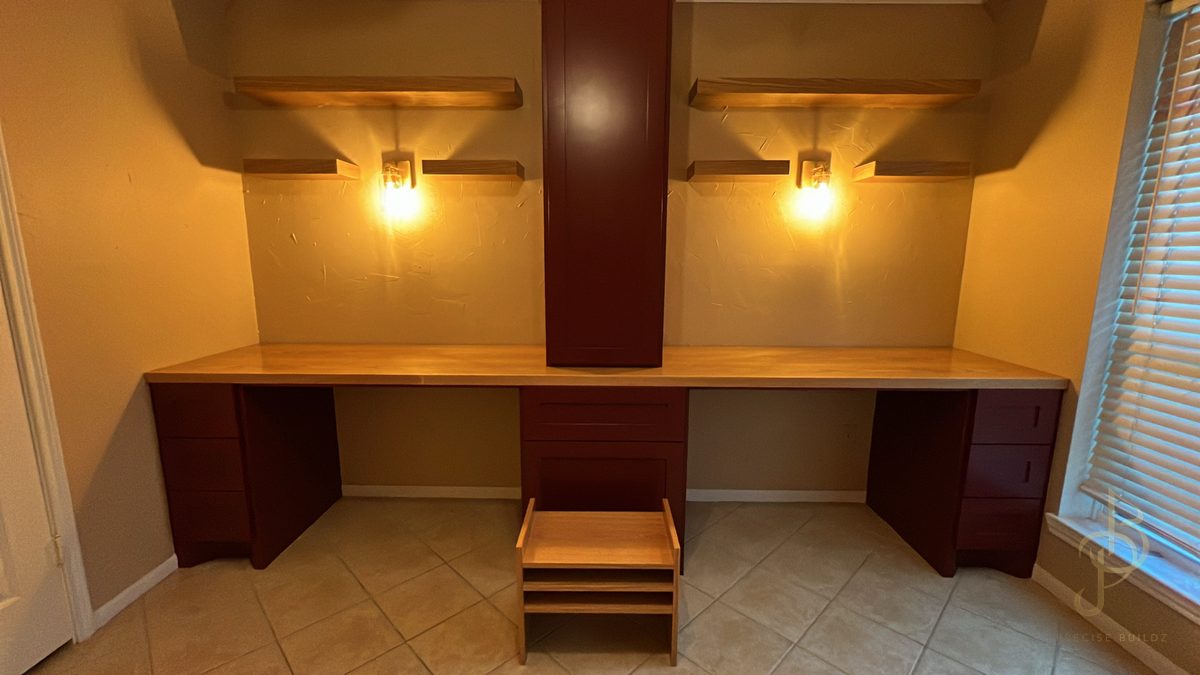 Custom office built-in with dual desks, deep red cabinetry, and floating shelves
