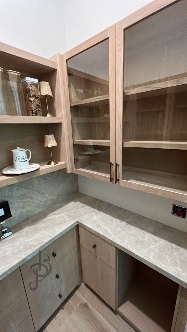 Open pantry shelves beside glass-front upper cabinets, with a stone counter and drawers below